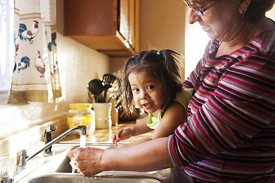 Woman washes toddler hands at kitchen sink Photograph by Laura Olivas