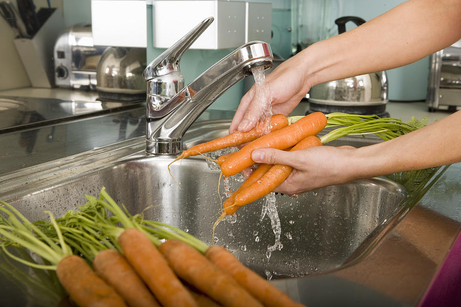Woman washing carrots at kitchen sink, close-up Photograph by Adam Gault