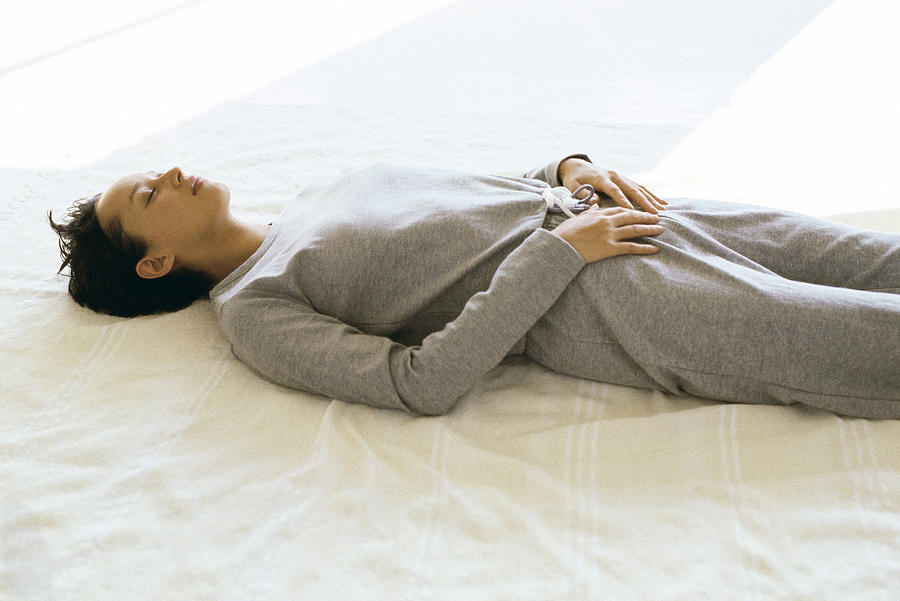 Woman wearing athletic wear lying on back with hands placed on lower abdomen Photograph by PhotoAlto/John Dowland