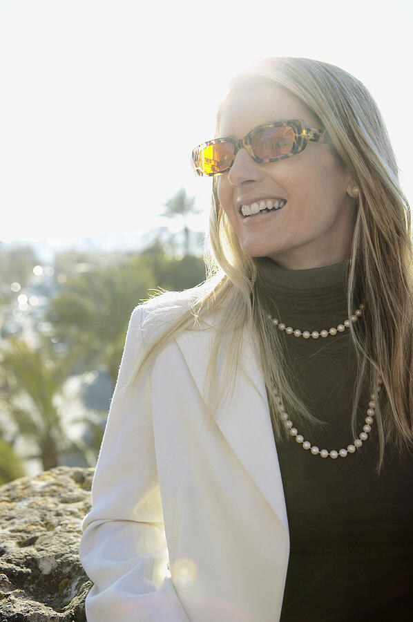Woman Wearing Sunglasses and a Pearl Necklace Looking Sideways Photograph by Digital Vision.