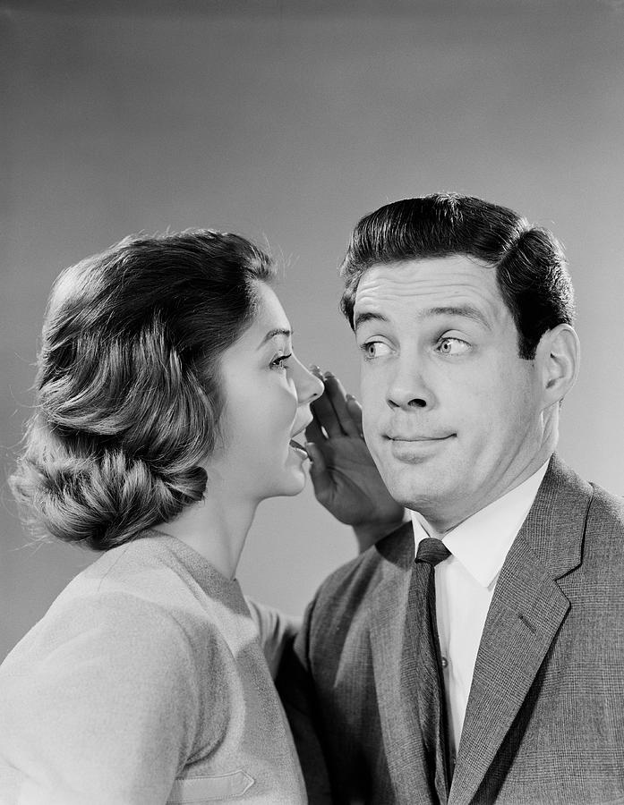 Woman whispering into mans ear, man pulling funny face. Photograph by H. Armstrong Roberts
