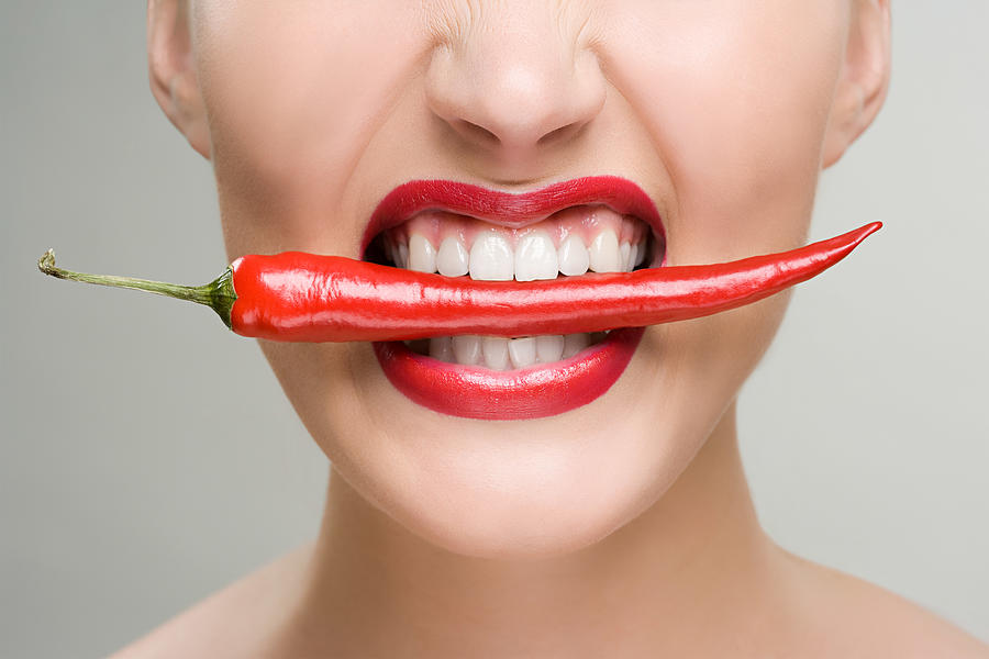 Woman with a red chili pepper between her teeth Photograph by Image Source