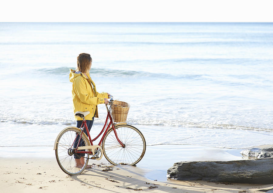 Woman with bike and yellow rain coat at beach. Photograph by Dougal Waters