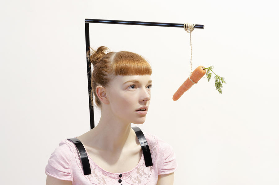 Woman With Carrot Dangling In Front Of Face Photograph by Tara Moore