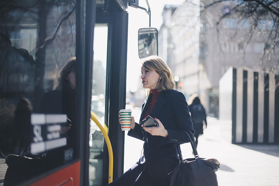 Woman with disposable cup and smart phone standing by bus in city on sunny day Photograph by Maskot