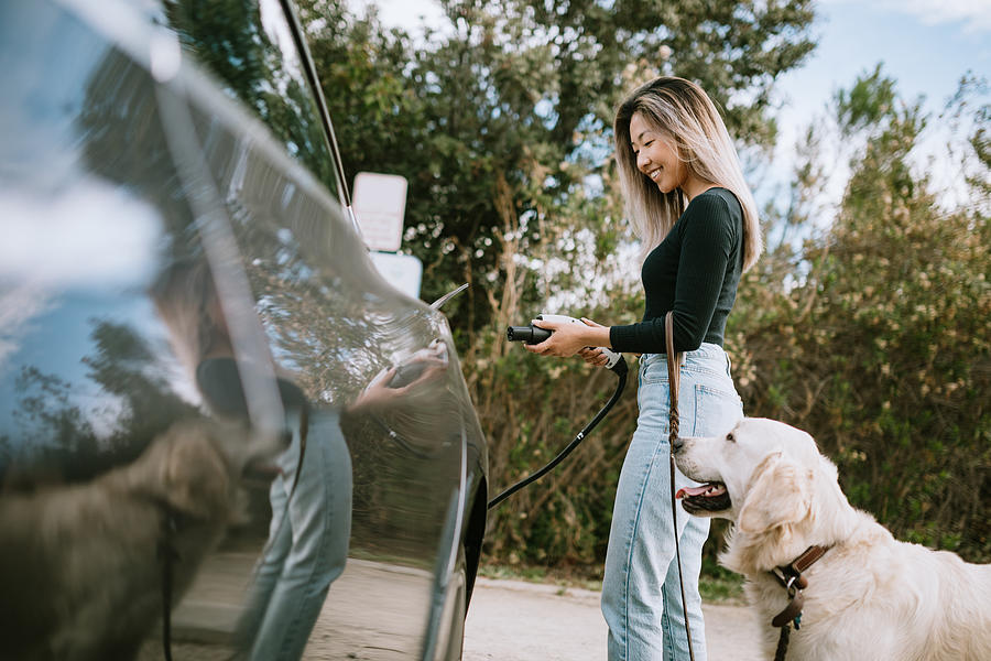 Woman With Dog Plugs In Electric Vehicle to Charge Photograph by RyanJLane