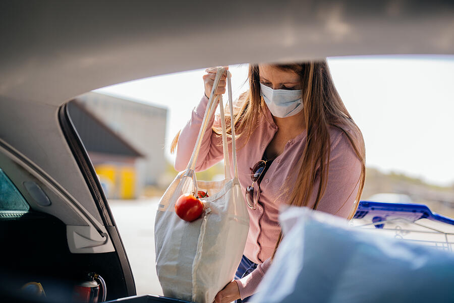 Woman with face mask loading car after shopping while covid-19. Photograph by Guido Mieth