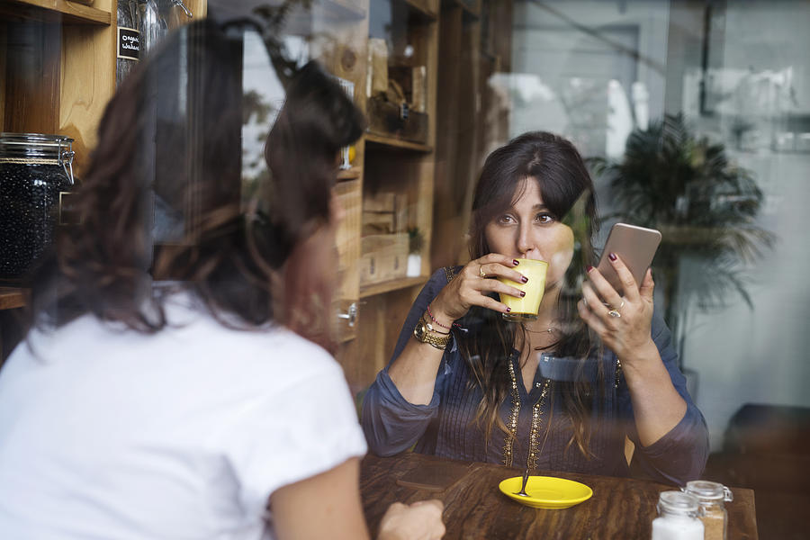 Woman with friend in a cafe holding smartphone and drinking coffee Photograph by Westend61