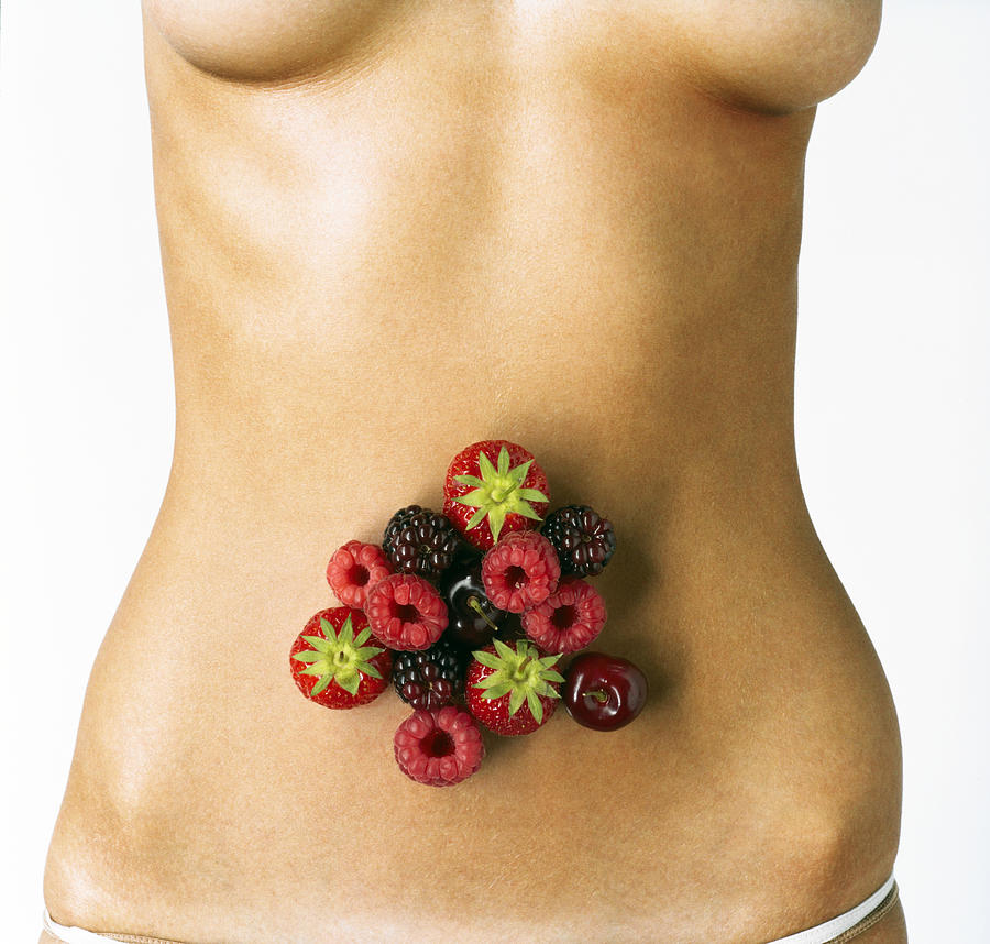 Woman with fruit over abdomen, mid section Photograph by Adam Gault