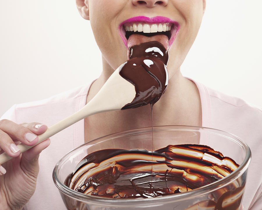 Woman with pink lipstick licking chocolate batter from wooden spoon Photograph by Chris Ryan