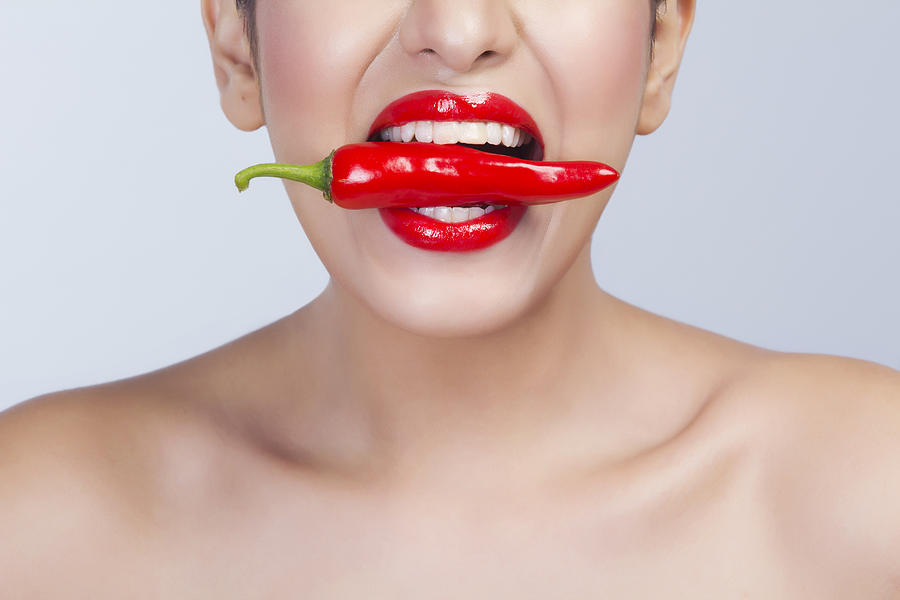 Woman with red pepper between her teeth Photograph by IndiaPix/IndiaPicture