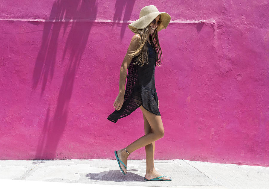 Woman with sun hat walking against bright wall Photograph by Nisian Hughes