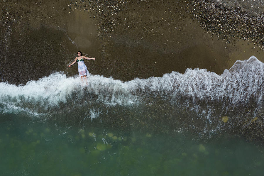 Woman with white dress resting on a sandy beach with braking waves on the shore. Overhead shot. Aerial drone photograph Photograph by Michalakis Ppalis
