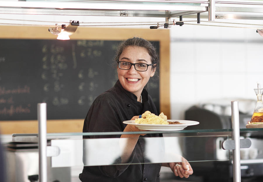 Woman working in restaurant kitchen, serving meal Photograph by Sigrid Gombert