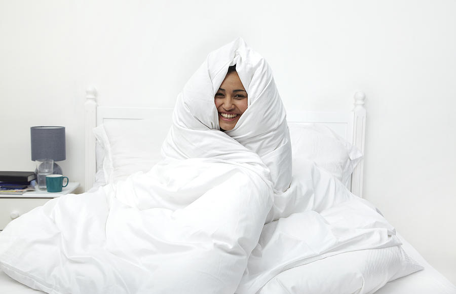Woman wrapped in duvet laughing Photograph by Flashpop