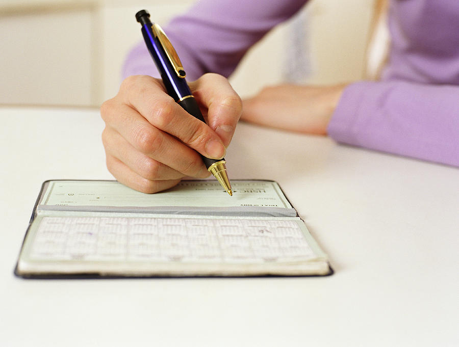 Woman writing in checkbook, close-up Photograph by Bruce Laurance