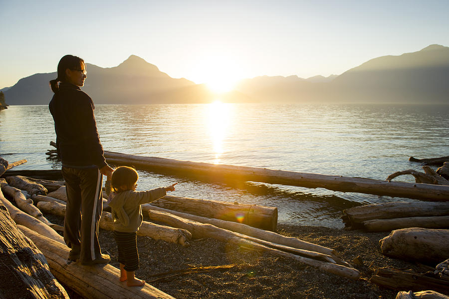 Woman w/small child pointing out to body of water at sunset Photograph by stockstudioX