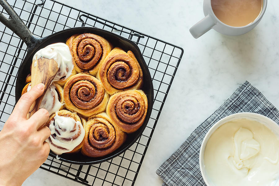 Womans Hand Spreading Frosting Across Cinnamon Rolls in Skillet Photograph by Viennetta