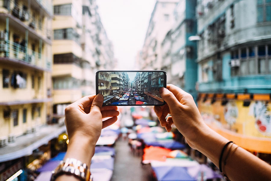 Womans hand taking a photo of local city street view in Hong Kong with smartphone Photograph by D3sign