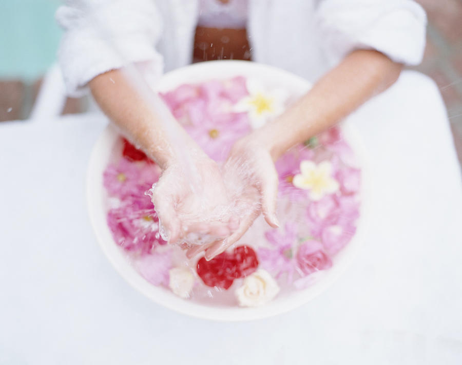 Womans hands in bowl of floating flowers Photograph by Getty Images