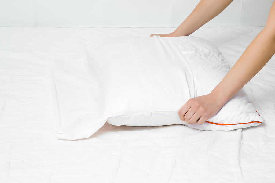 Womans hands on mattress surface changing white cotton cover on pillow. Regular bed linen change. Closeup. Photograph by FotoDuets
