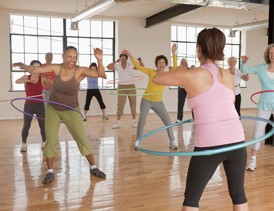 Women exercising plastic hoops in fitness class Photograph by Ariel Skelley