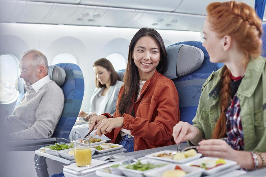 Women friends eating dinner and talking on airplane Photograph by Caia Image