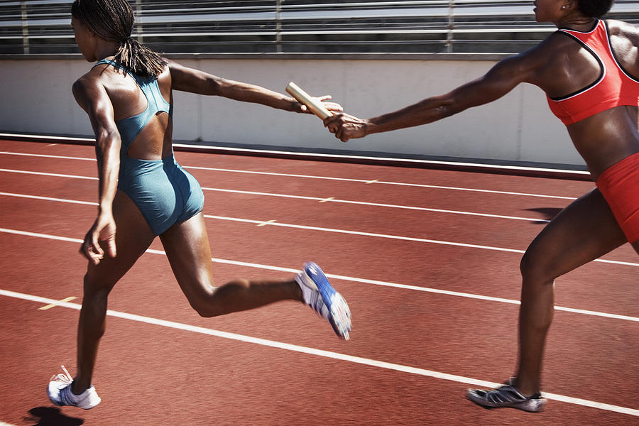 Women passing baton to each other during race Photograph by Jupiterimages