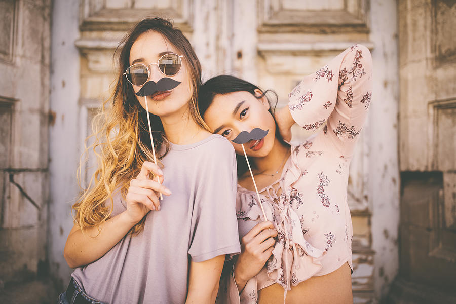 Women playing with mustaches on sticks in city streets Photograph by Wundervisuals