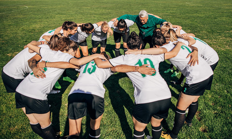Women soccer team and coach hugging Photograph by South_agency