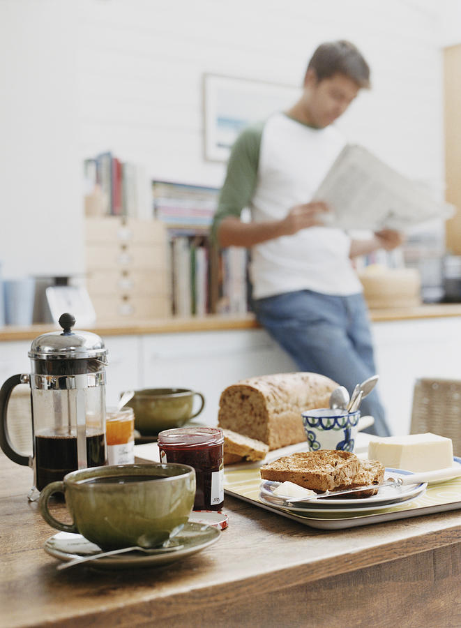 Wooden Table With Breakfast, Man Reading Newspaper in the Background Photograph by Digital Vision.