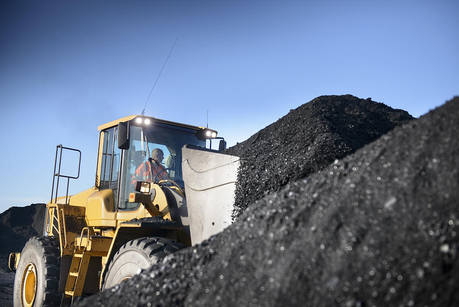 Worker operating digger with pile of coal at surface coal mine Photograph by Monty Rakusen