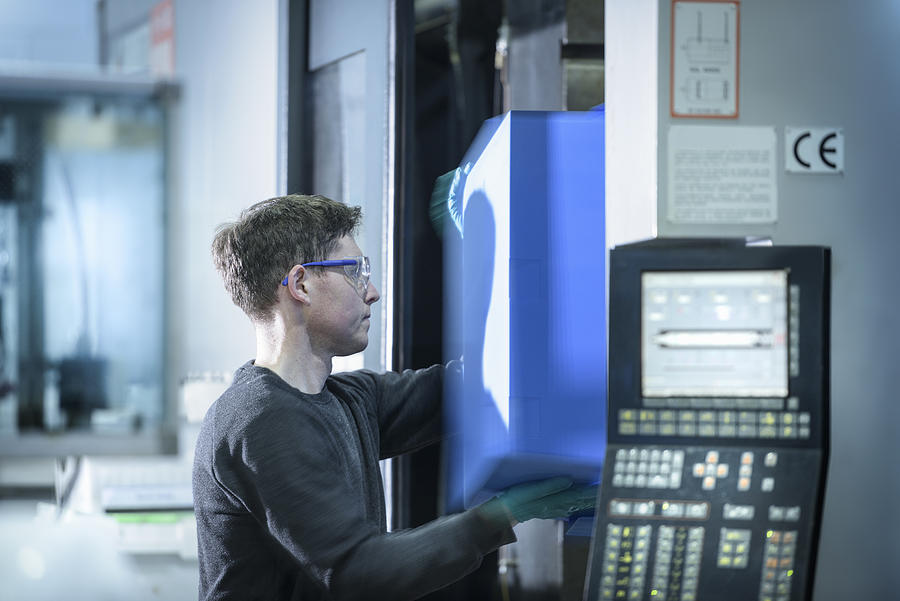 Worker removing plastic part from injection moulding machine in plastics factory Photograph by Monty Rakusen