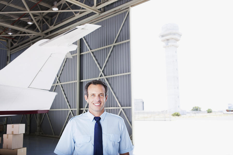 Worker standing with airplane in hangar Photograph by Martin Barraud