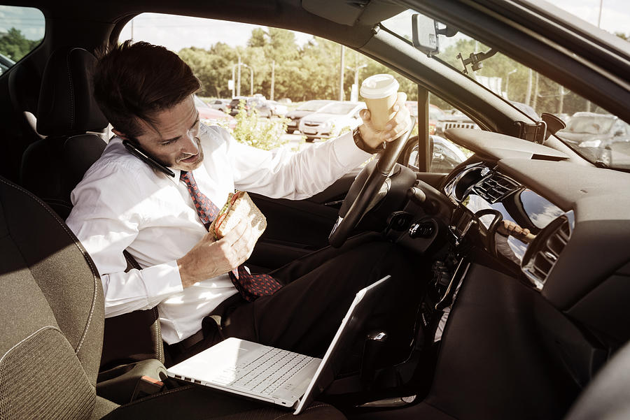 Working businessman eating inside car Photograph by D-Keine