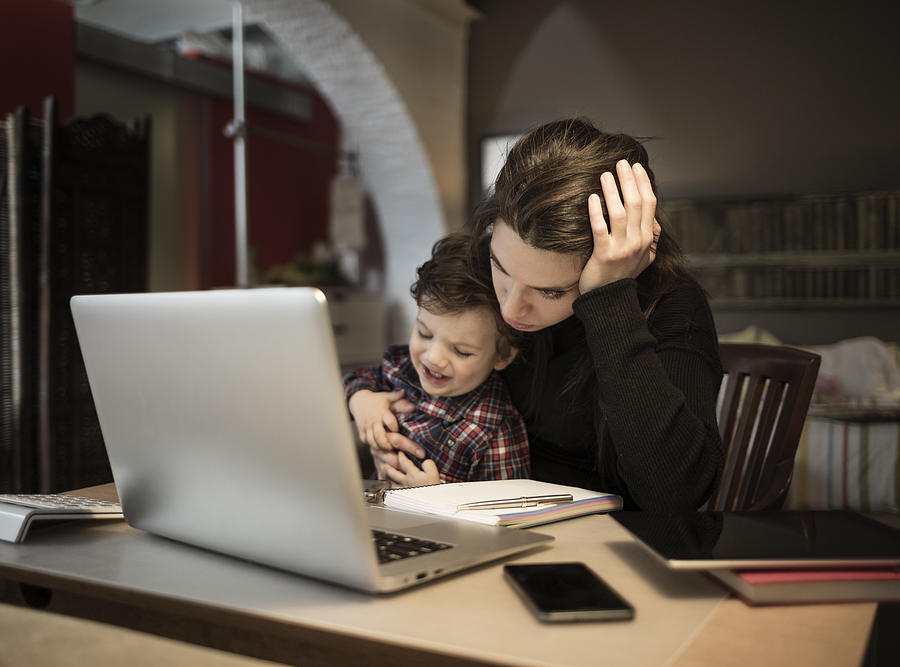 Worried woman working at home and holding her crying little son Photograph by Aluxum