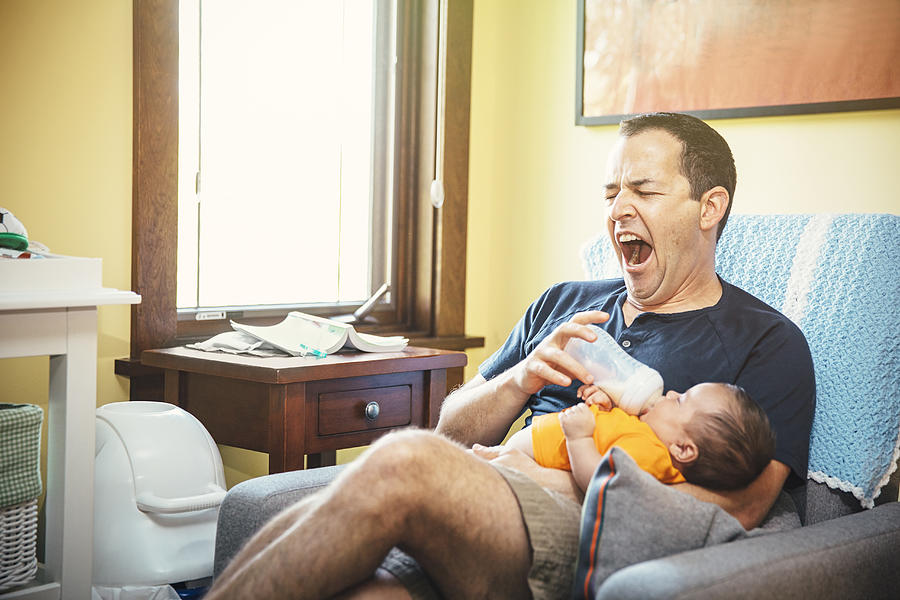 Yawning Caucasian father feeding baby boy in living room Photograph by Inti St Clair