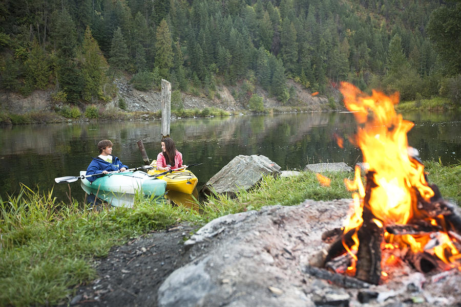 Young adult couple camping with a camp fire and kayaks on a beautiful summer evening. Photograph by Patrick Orton