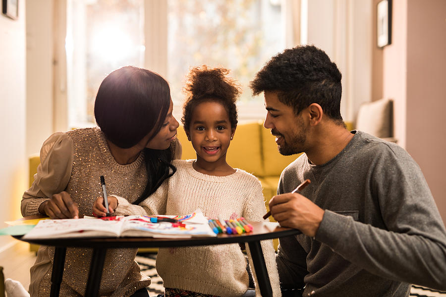 Young African American family drawing at home and enjoying in creative time together. Photograph by Skynesher
