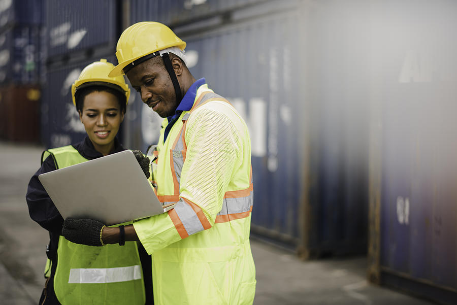 Young African american men and woman worker Check and control loading freight Containers by use computer laptop at commercial shipping dock felling happy. Cargo freight ship import export concept Photograph by Niphon Khiawprommas