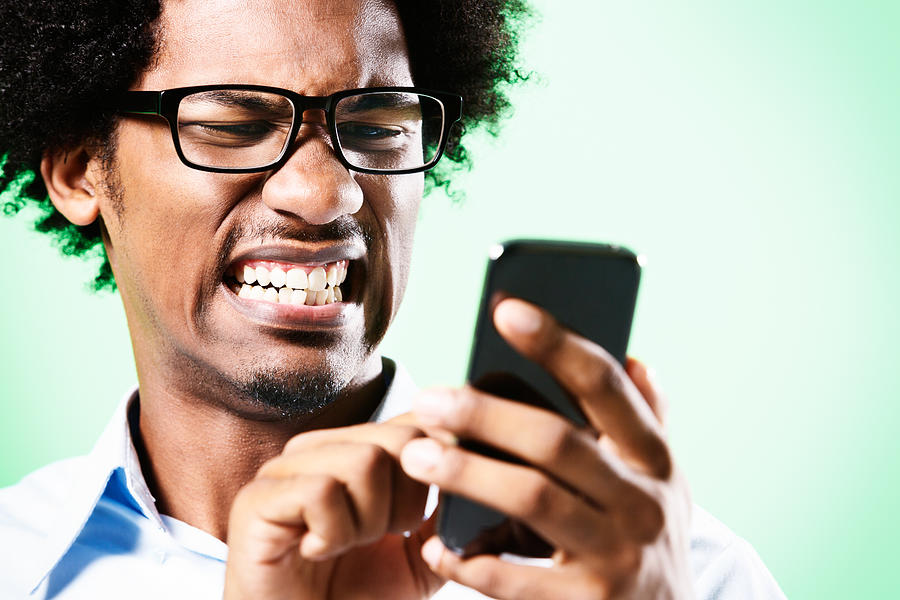 Young afro-haired nerd grimaces at cellphone he holds Photograph by RapidEye