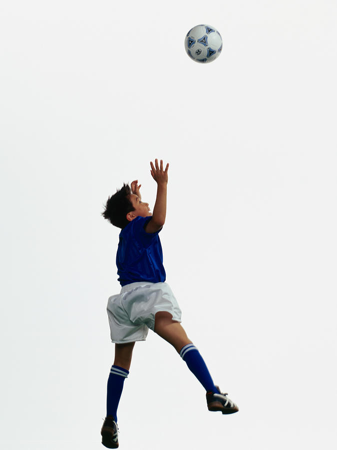 Young Asian boy jumping to head soccer ball in mid-air Photograph by Dex Image