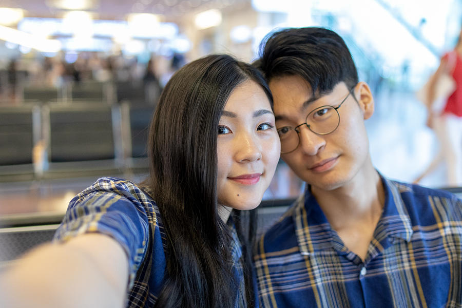 Young Asian couple taking selfie pictures in airport Photograph by Satoshi-K
