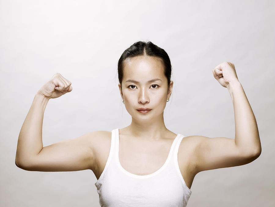 Young asian woman flexing her muscles Photograph by Ballyscanlon