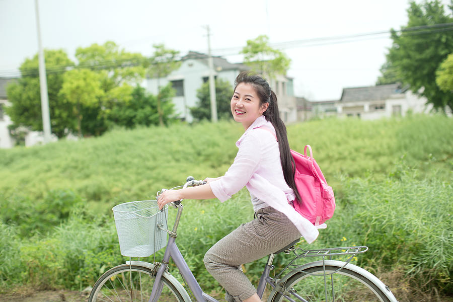 Young asian woman riding bicycle through country rapeseed field Photograph by Xia Yuan