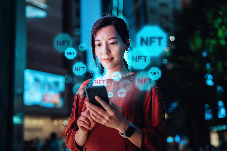 Young Asian woman using smartphone in downtown city street at night, working with blockchain technologies, investing or trading NFT (Non-Fungible Token) on cryptocurrency, digital asset, art work and digital ledger Photograph by D3sign