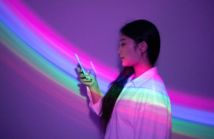 Young Asian woman using smartphone on rainbow background Photograph by Qi Yang