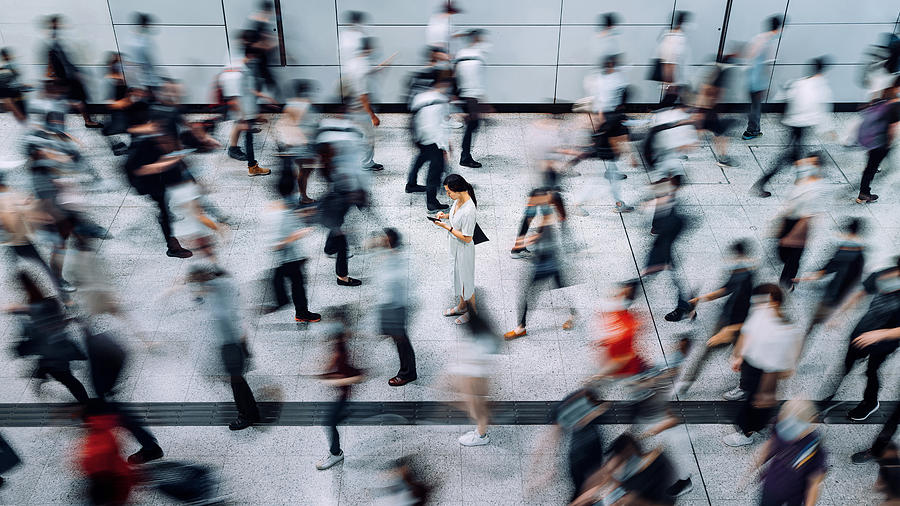 Young Asian woman using smartphone surrounded by commuters rushing by in subway station during office peak hours in the city Photograph by D3sign