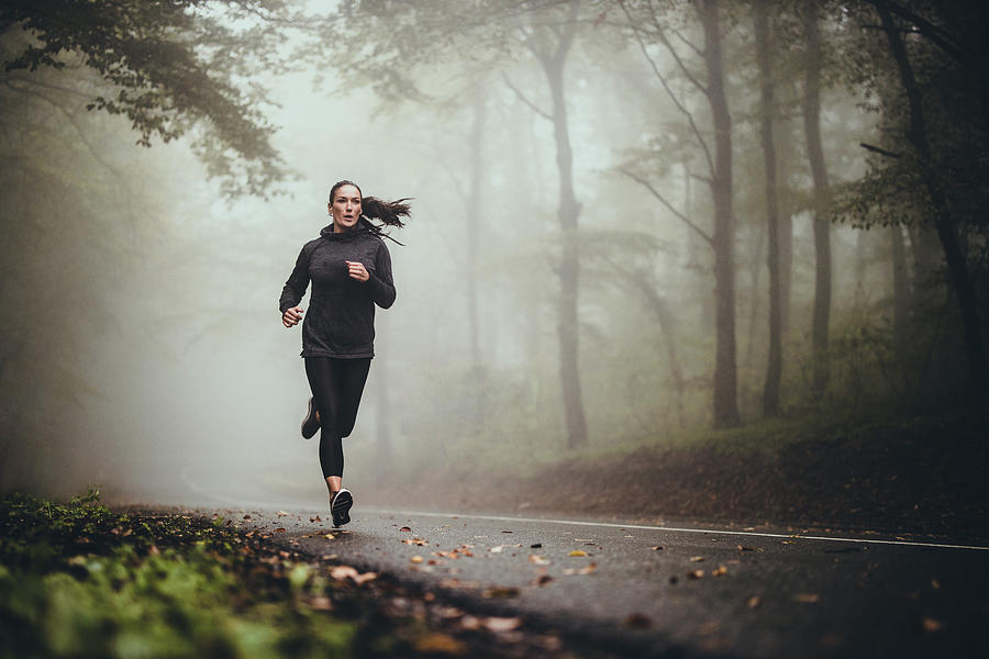 Young athletic woman jogging on the road in foggy forest. Photograph by Skynesher