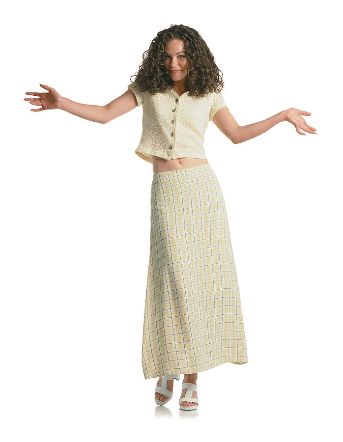 Young Beautiful Brunette Teenage Girl With Curly Hair Wearing A Cream Plaid Skirt And Cream Short Shirt Steps Toward The Camera And Gives A Slight Smile As She Holds Her Hands And Arms Out To The Side Photograph by Photodisc
